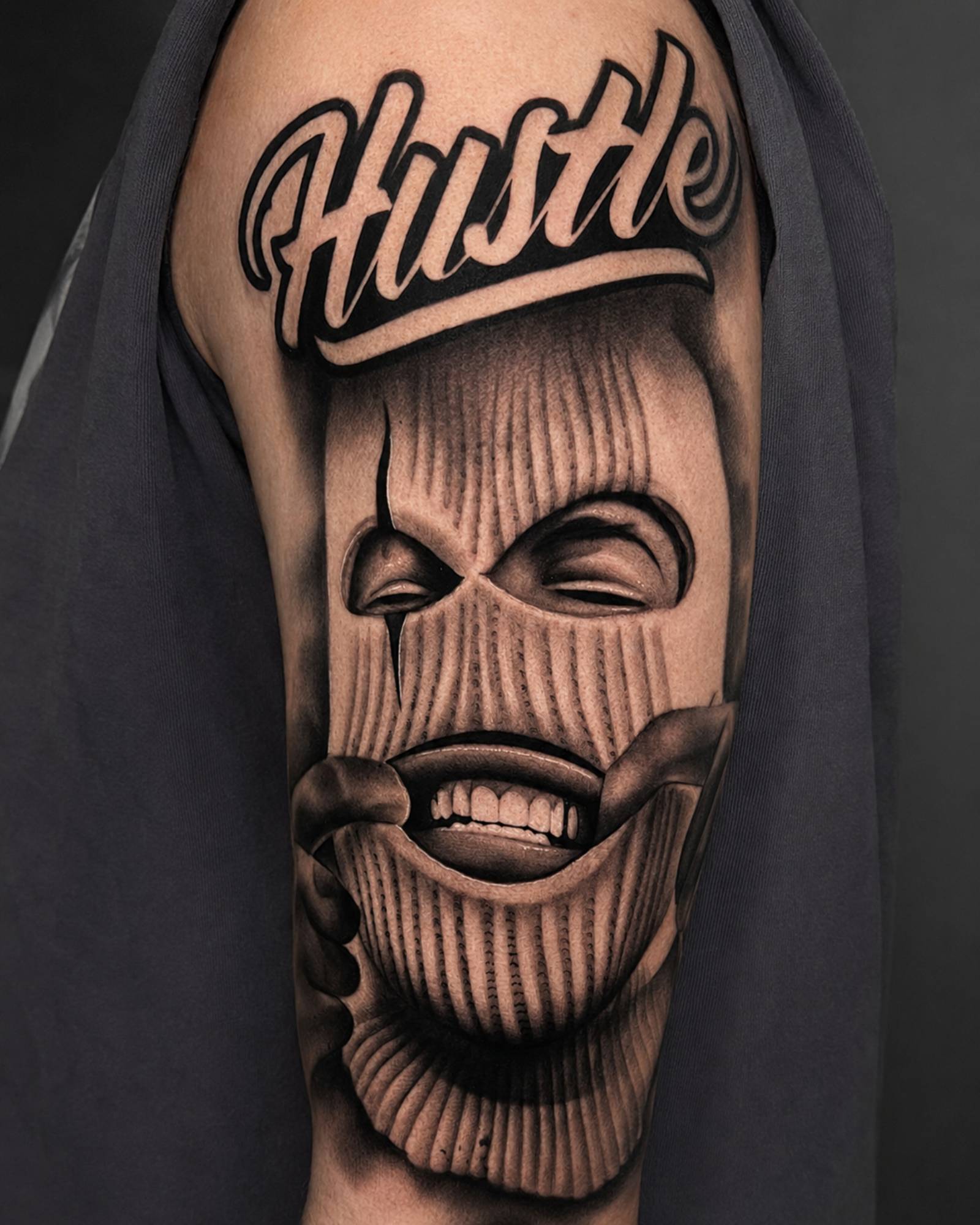 Black Grey Hustle Masken Tattoo am Oberarm in Kassel